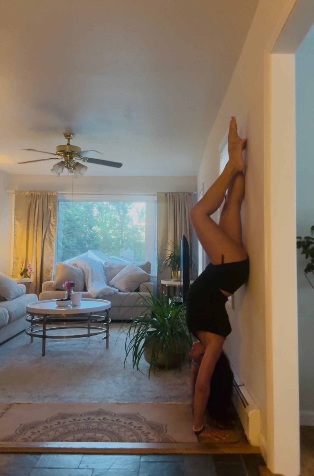 Darlene Cook in a wall-assisted handstand in the living room, mandala rug below