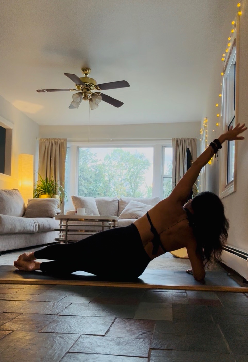Darlene Cook in side plank on the mat, fairy lights along the window behind her